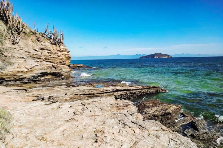 Imagem da paisagem com rochas e o mar se encontrando com o céu ao fundo na Praia da Tartaruga em Búzios