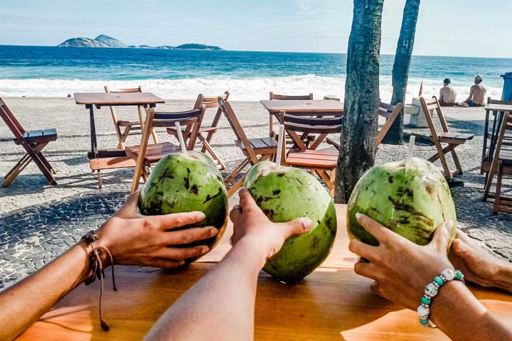 Imagem de três pessoas tomando água de coco em um quiosque na Praia de Ipanema