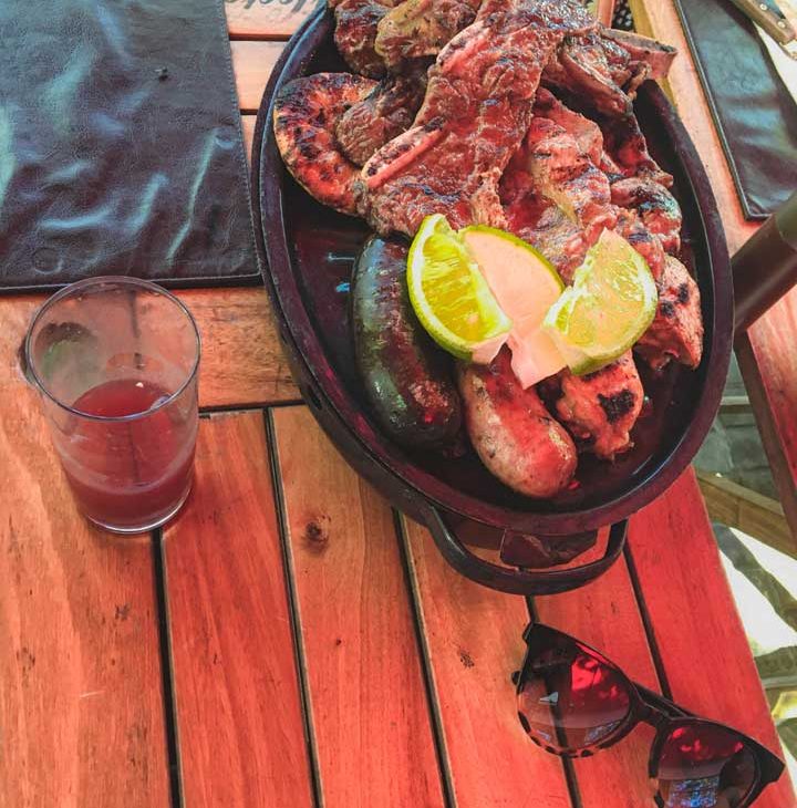 Foto da Parrilla Uruguaia, um churrasco com uma variedade de cortes de carne, acompanhado por um copo de sangria.