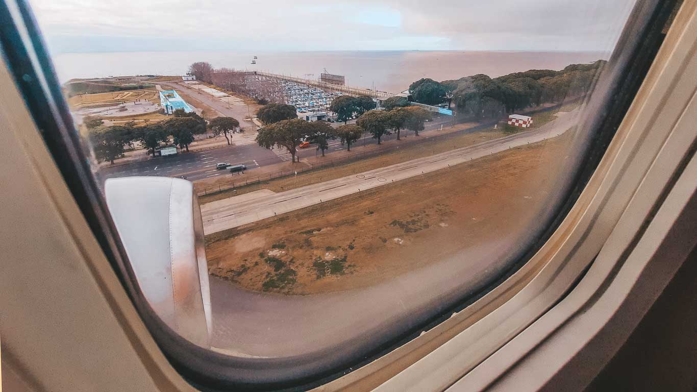 Vista da janela de um avião sobrevoando uma estrada costeira de Buenos Aires, com a asa do avião em primeiro plano, capturando o momento da viagem e uma das principais maneiras de como ir de Buenos Aires para Montevidéu.