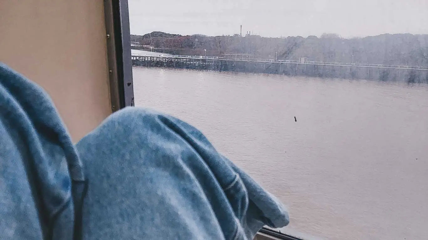 Imagem de uma pessoa sentada na janela do ferry em um dia nublado, uma das formas mais práticas de como chegar em Colonia del Sacramento.