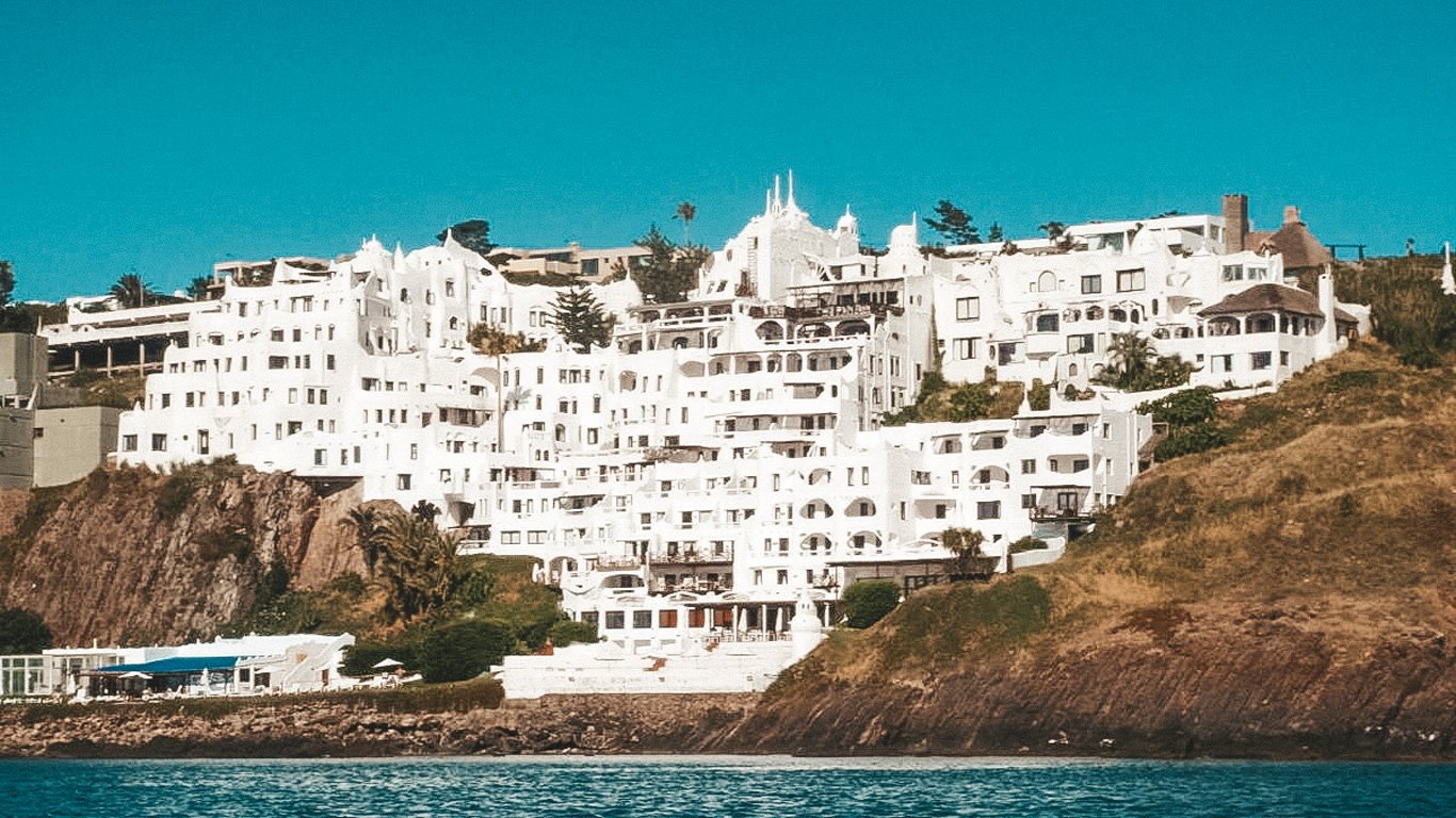 Casapueblo, o icônico hotel e museu em Punta del Este, resplandece sob o sol, com sua arquitetura branca e desenhos únicos se destacando sobre o penhasco rochoso à beira-mar.