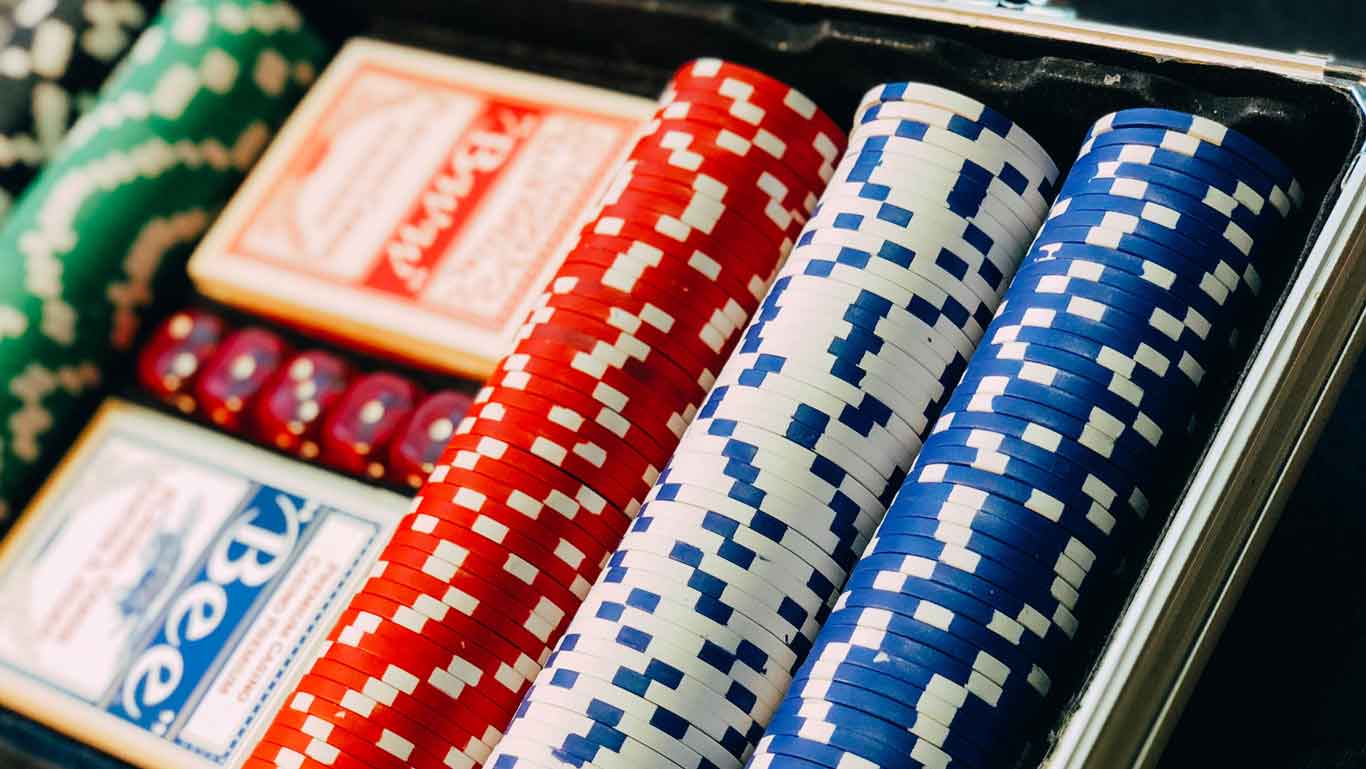 Visão aproximada de fichas de pôquer coloridas empilhadas em fileiras em um estojo com baralhos de cartas, capturando a emoção dos jogos do Enjoy Punta del Este Casino, um dos principais pontos turísticos de Punta del Este.