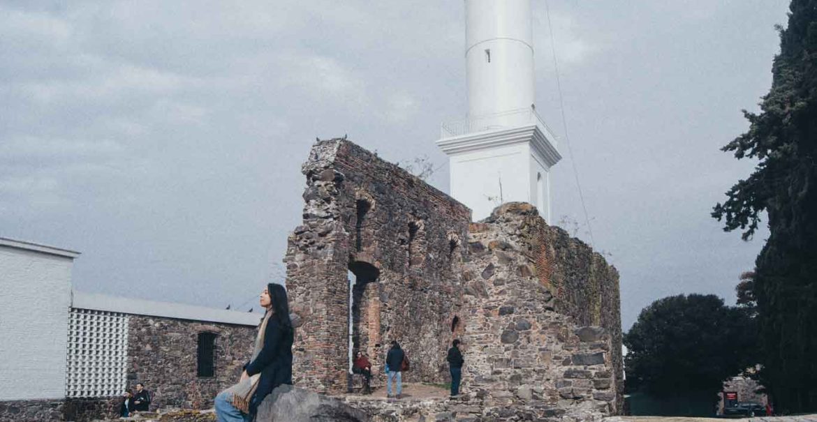 Uma mulher está sentada junto às ruínas do convento, localizadas ao lado do Farol de Colonia do Sacramento.