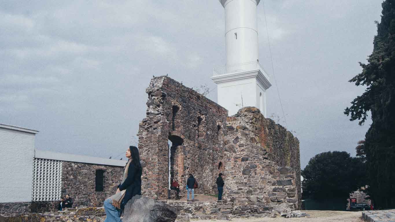 Uma mulher está sentada junto às ruínas do convento, localizadas ao lado do Farol de Colonia del Sacramento.