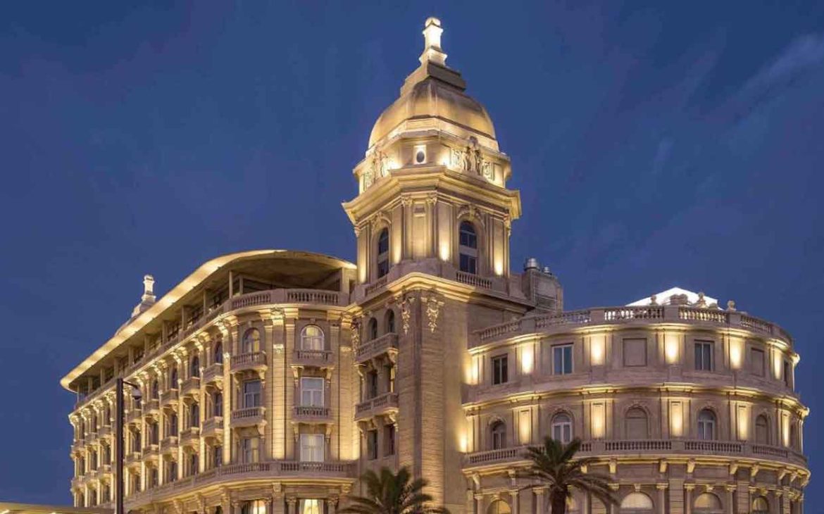 A imagem mostra o Sofitel Montevideo Casino Carrasco & Spa iluminado à noite. Este hotel luxuoso destaca-se pela sua arquitetura elegante e clássica, com detalhes iluminados que realçam suas linhas sofisticadas contra o céu noturno.