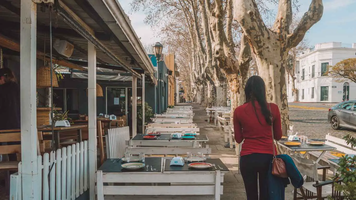 Uma mulher caminhando pela calçada de Colonia del Sacramento, onde se deparamos com numerosas cadeiras de um restaurante.