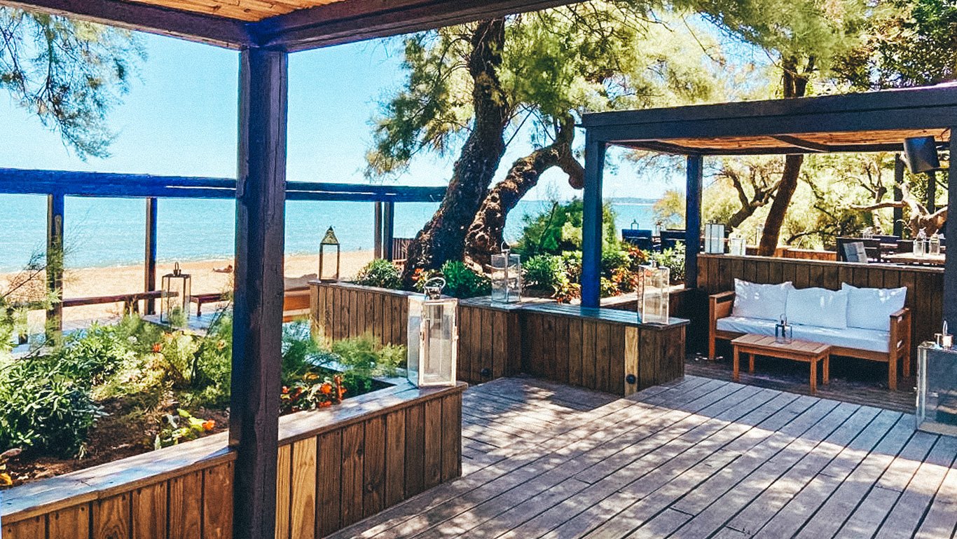 Área de descanso ao ar livre do Serena Hotel em Punta del Este, com sofás confortáveis e decoração rústica em uma varanda de madeira, oferecendo uma vista deslumbrante da praia tranquila e do mar azul ao fundo.