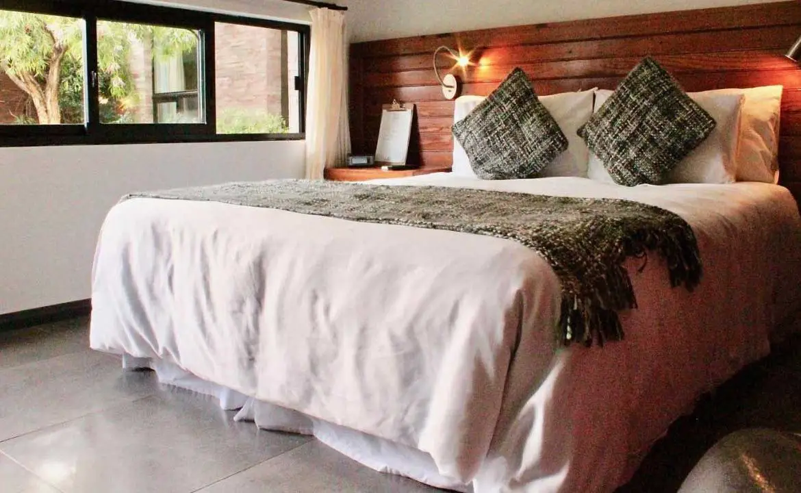 Quarto da Posada Boutique Las Terrazas em Colonia del Sacramento com detalhes de madeira e uma cama de casal com lençóis brancos.