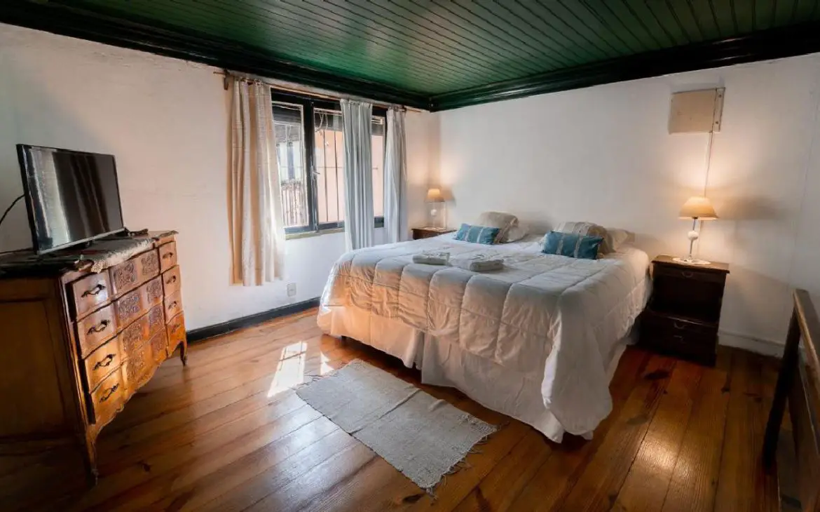Um quarto modesto na Posada de la Flor em Colonia del Sacramento, caracterizado por móveis antigos e uma cama com lençóis brancos.