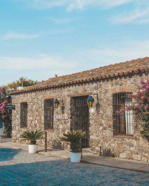 Fachada de pedra do Charco Hotel, o melhor hotel para ficar em Colonia del Sacramento, com flores ramificando pela parede. 